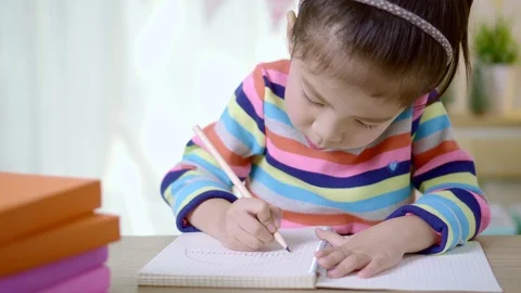 Kid's creativity, Child little asian girl writing in the book on the desk Stock Footage