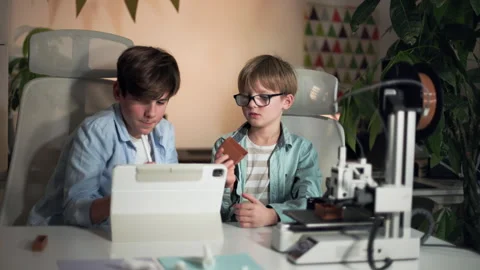 Kids discuss a 3D printed part and make adjustments on a laptop to print other Stock Footage 335379327