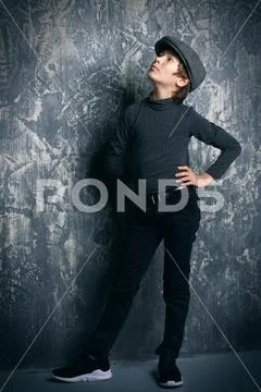 Kid's fashion. Modern boy posing in dark clothes and hat at studio. Clothes Stock Photos