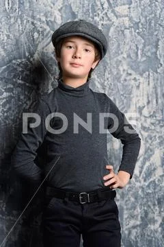 Kid's fashion. Modern boy posing in dark clothes and hat at studio. Clothes Stock Photos