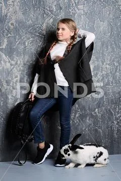 Kid's fashion. Modern girl is posing in dark clothes and hat with rabbit at s Stock Photos