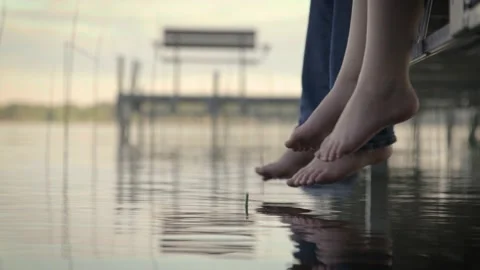 Kids feet dangling over a lake while sitting on a dock at dusk. Stock Footage