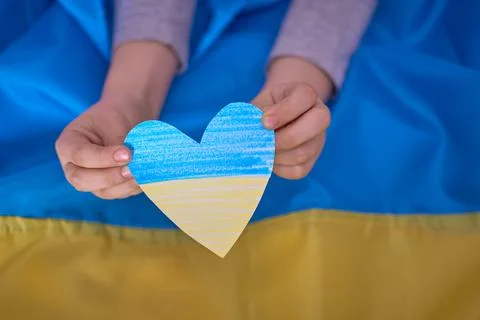 Kids hands holding yellow-blue paperhearts on Ukrainian flag background Stock Photos