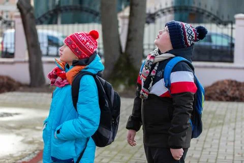 Kids look up at the sky while standing on a sidewalk near trees in winter o.. Stock Photos