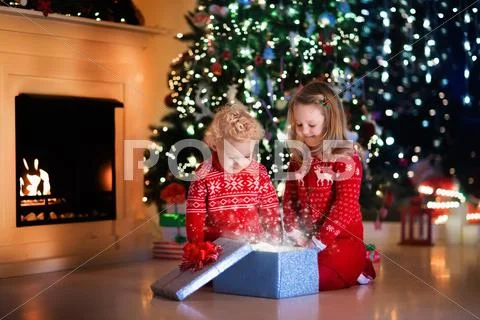 Kids opening Christmas presents at fireplace Stock Photos