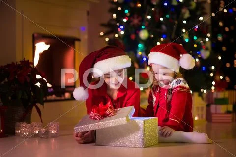 Kids opening Christmas presents at fireplace Stock Photos