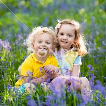 Kids playing in blooming garden with bluebell flowers Stock Photos
