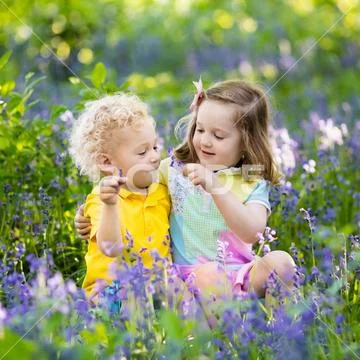 Kids playing in blooming garden with bluebell flowers Stock Photos