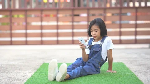 Kids playing smartphone on artificial grass on ground area of home  Stock Footage 129581052