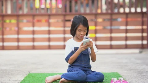 Kids playing smartphone on artificial grass on ground area of home  库存影片 129581235