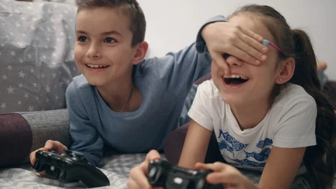Kids playing video games. Brother close eyes sister. Children have fun together Stock Footage