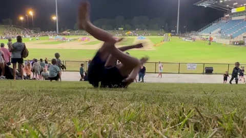 Kids rolling down a grass hill at the end of a Monster Trucks show Vídeos de archivo 229399658