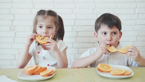 Kids in self-isolation. Boy and girl eating orange. Children sitting at home Stock Footage 128431759