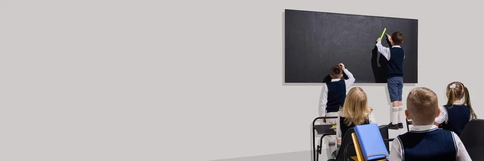Kids standing at blackboard, solving problem using ruler while classmates watch Stock Photos