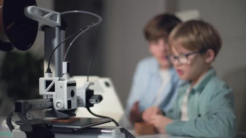 Kids at a table with a working 3D printer, observing and operating it Stock Footage 335377254
