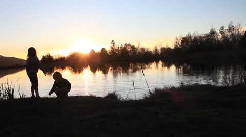 Kids throwing rocks into the lake at sunset. Stock Footage 32209630