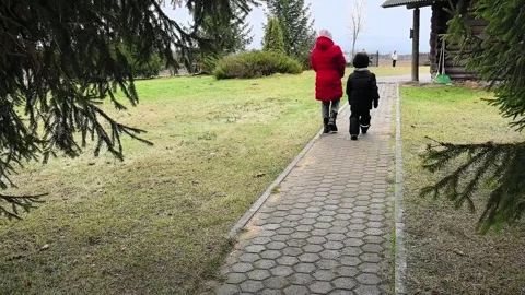 Kids walking on a path in a park during a cloudy day with trees around and a bui Stock Footage 330155121