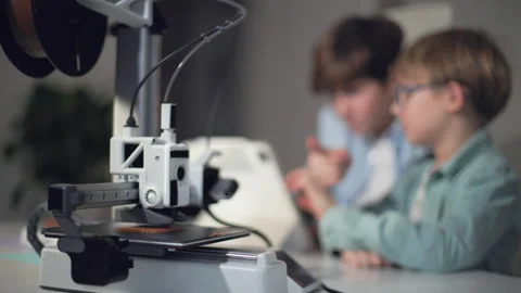 KIds watch a 3D printer in operation in the foreground Stock Footage 335376590