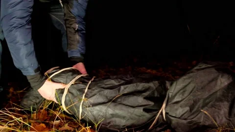 Killer and corpse.  Maniac and victim in a black bag in a dark park. Vidéo 165383006