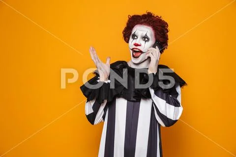 Kind clown man 20s wearing black costume and halloween makeup talking on smar Stock Photos