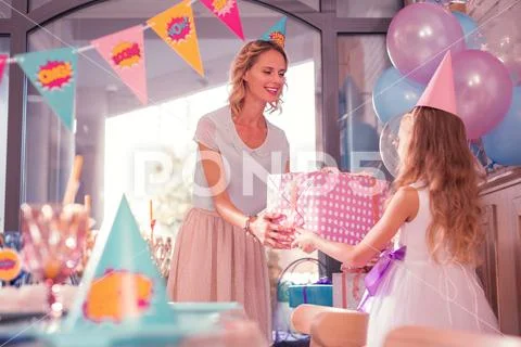Kind woman smiling and giving birthday present to her daughter Stock Photos