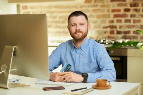 A kind young man posing with his credit card in front of the computer. Stock Photos