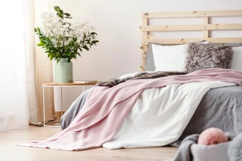 King-size bed with grey sheets and pink blanket standing in bright bedroom in Stock Photos