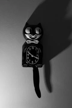 A Kit Cat Clock in dramatic lighting hangs on a wall. Stock Photos