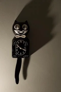 A Kit Cat Clock in dramatic lighting hangs on a wall. Stock Photos