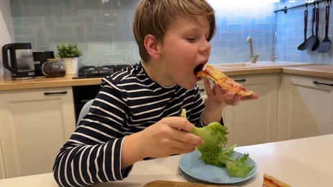 In the kitchen, the boy happily eats pizza Stock Footage 302928503