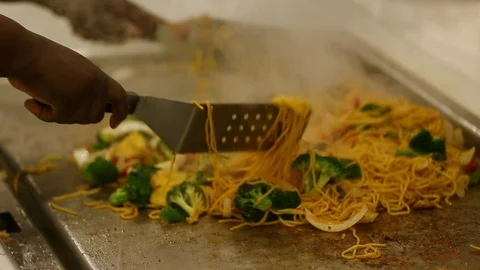 Kitchen chef makes chow mein stir fry on large flat griddle stove with spatul Stock Footage 112950693