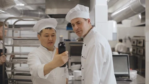 Kitchen cooks studying bottle of new product in industrial kitchen Stock Footage 125051250