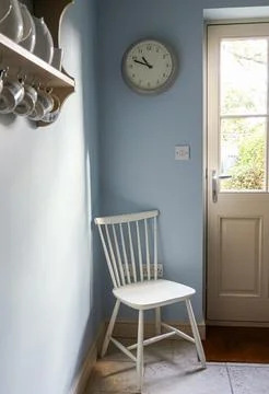 Kitchen corner with wall clock, white chair, and natural light entering doo.. Stock Photos
