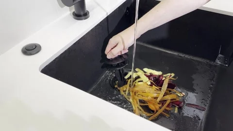 Kitchen disposer process. Hand cleaning vegetable peel leftovers in sinkhol.. Stock Footage 320185076