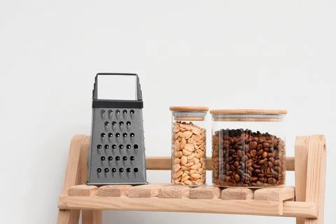 Kitchen grater, peanuts, and coffee beans in glass jars on wooden shelf, food Stock Photos