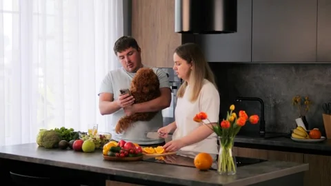 In kitchen happy couple is preparing breakfast with dog, looking at recipe on Stock Footage 277109427