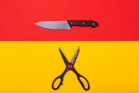 Kitchen knife and scissors lie isolated on a yellow-red background Stock Photos