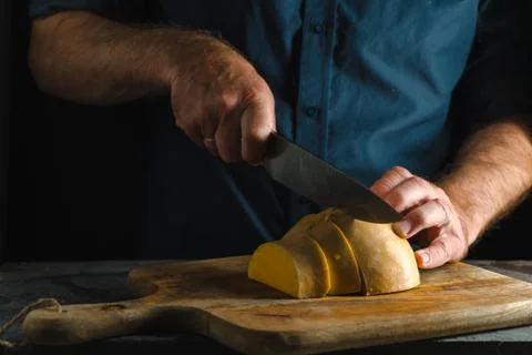 Kitchen knife cuts half a pumpkin into strips on a wooden board Stock Photos