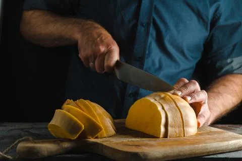 Kitchen knife cuts half a pumpkin on a wooden board close-up Stock Photos