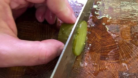 A kitchen knife slices pickled cucumber into thin rounds on a wet wooden cu.. Stock Footage 346166295
