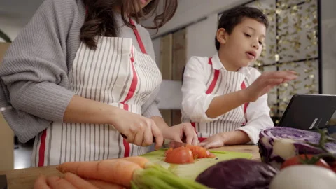 In the kitchen: Mother cutting tomato while her son watches and learns. Cooki Stock Footage 150675969