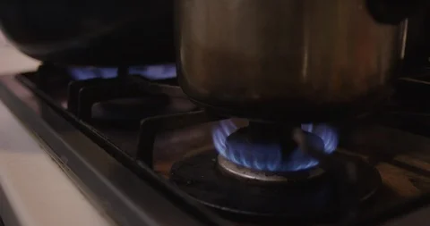 Kitchen pots and pans on stove top gas burner eyes with hot blue flames CU Stock Footage 112937752