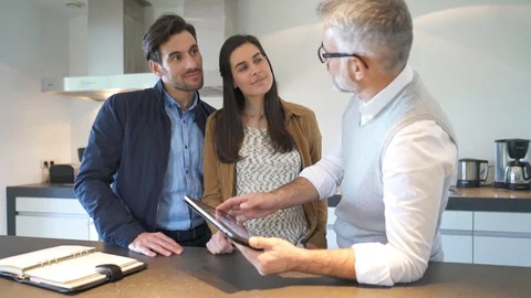 Kitchen rep going through specs on tablet with couple in showroom Stock Footage 99675650