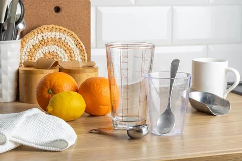 A kitchen scene with oranges, measuring cups, and a spoon on a wooden table. Stock Photos