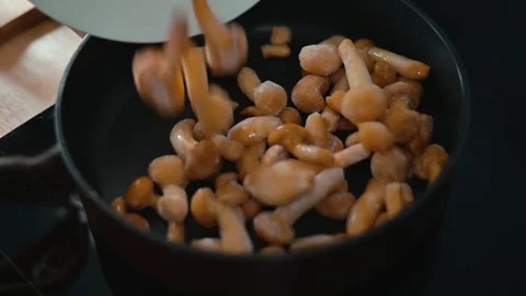 In a kitchen setting, mushrooms are being added to a hot pan containing oil. Stock Footage 339094503