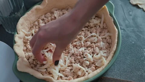 In a kitchen setting, a person sprinkles cheese over a chicken pie filling Video stock 339094551