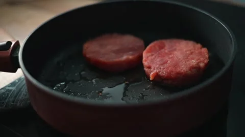 In a kitchen setting, two patties are placed in a frying pan with some oil. A Stockbeeldmateriaal 338304060