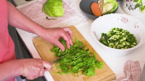 In a kitchen setting, a woman cuts lettuce leaves on a cutting board. She o.. Stock-Footage 337059754