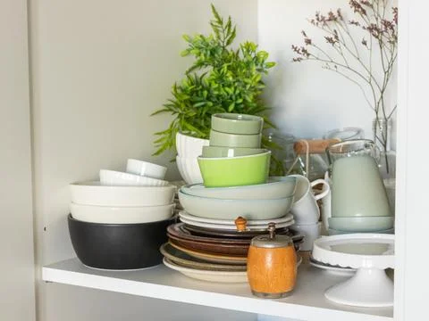 A kitchen shelf with diverse stacks of ceramic plates, bowls, and cups in neu Stock Photos