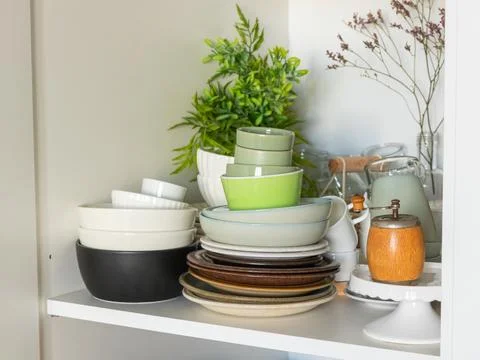 A kitchen shelf with diverse stacks of ceramic plates, bowls, and cups in neu Stock Photos
